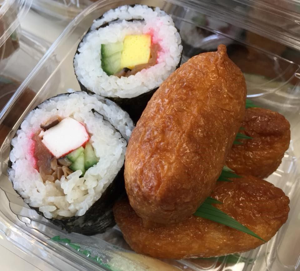 Sushi rolls and tempura-like pastries in a clear takeout container with green garnish.