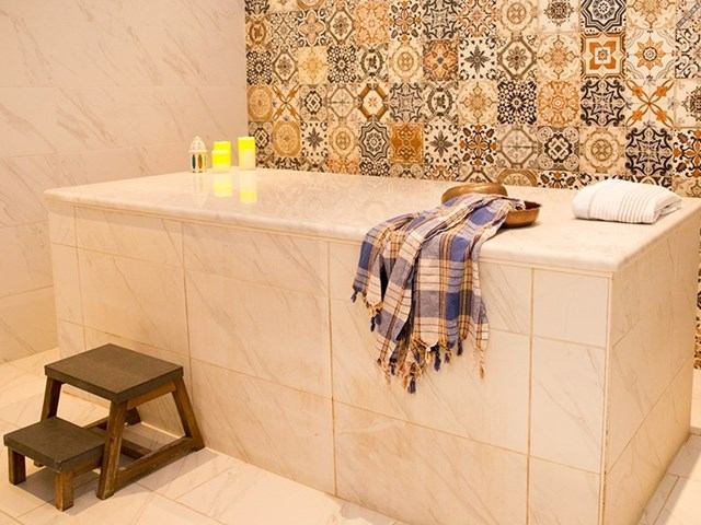 Marble massage table with towels, candles, and patterned tile wall in spa setting.