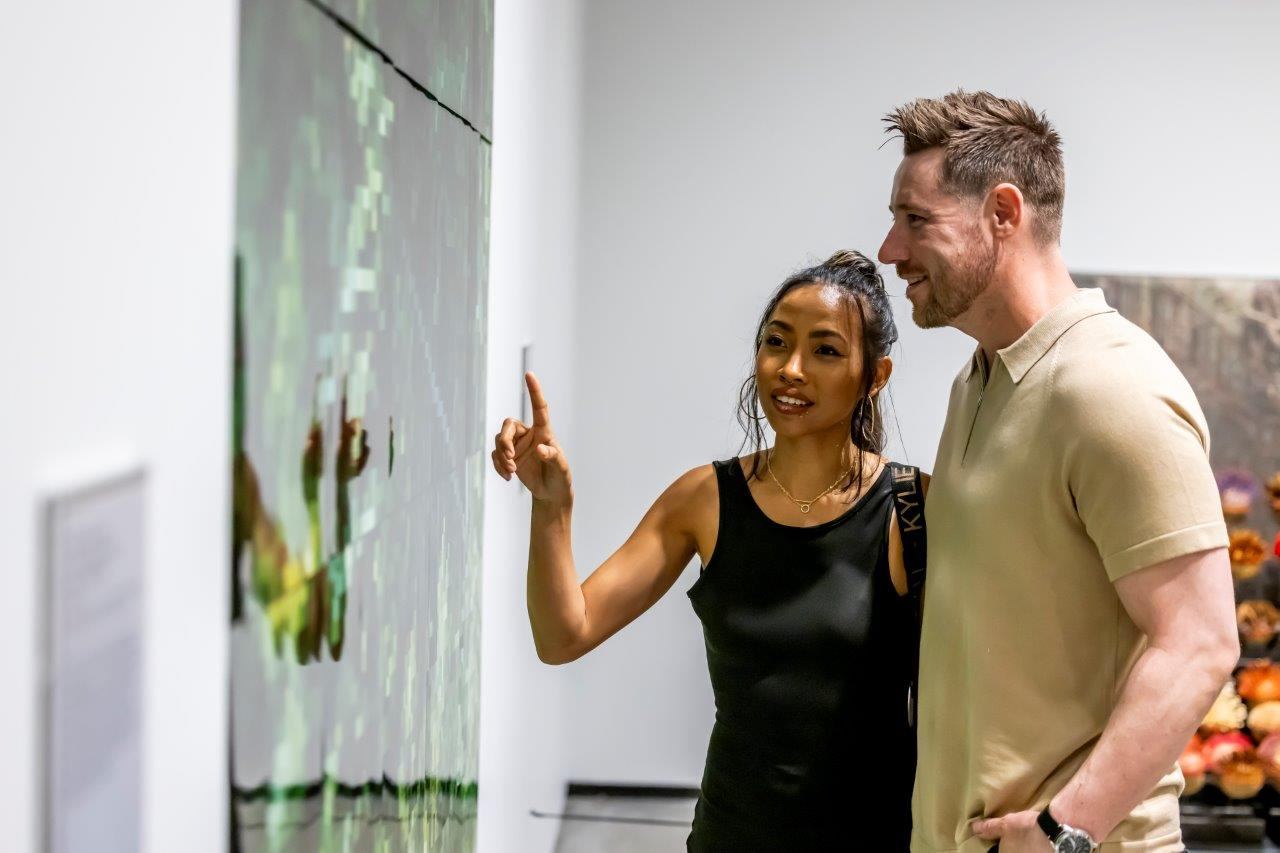 Gallery visitors examine artwork as one person points toward the display.