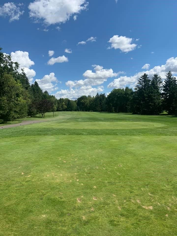 Green fairway lined with trees and blue sky at Victoria Golf Course and Driving Range.