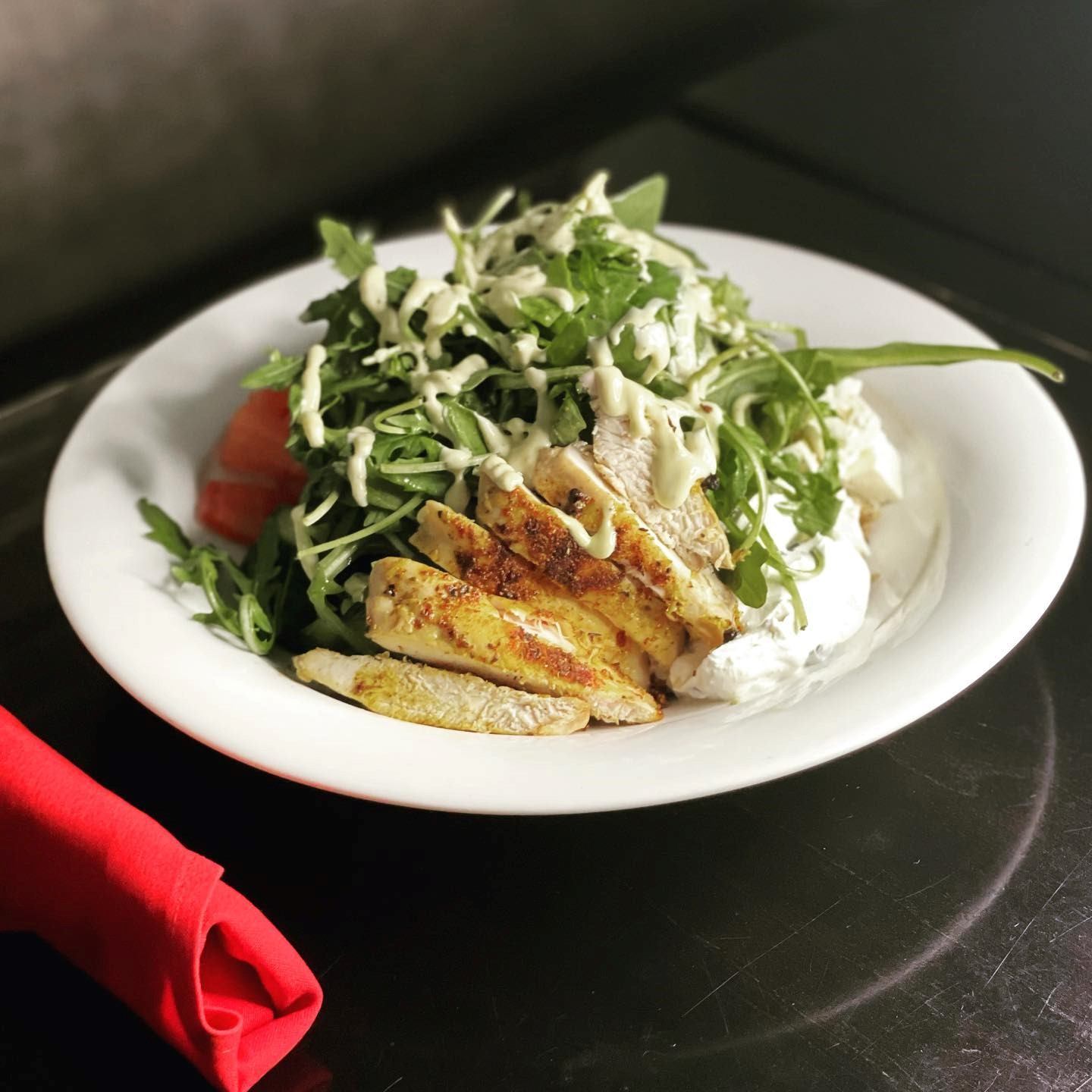 Salad topped with grilled chicken, leafy greens, and dressing on a white plate.