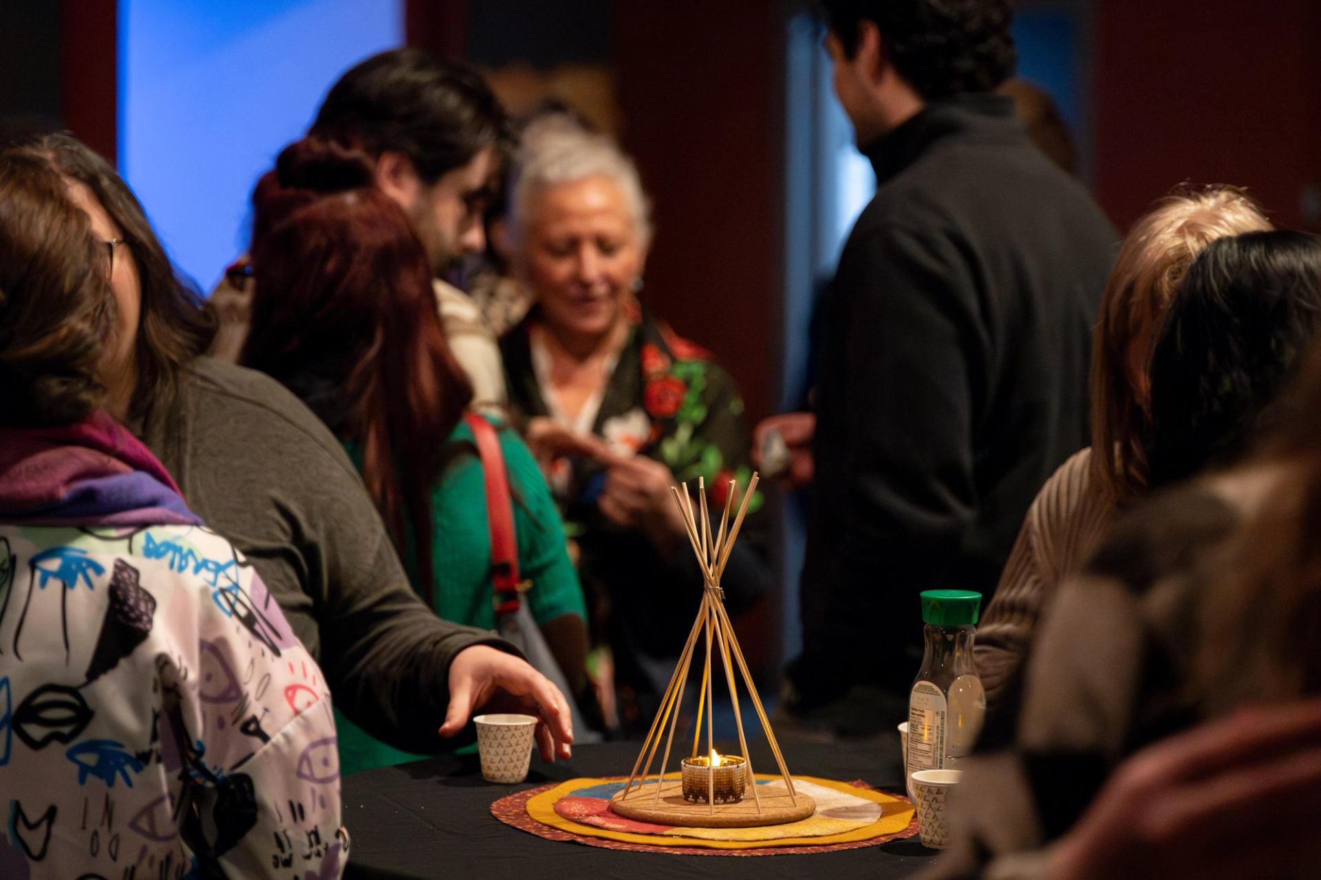 People gathered around a table with a small teepee-style display and candle at an event.