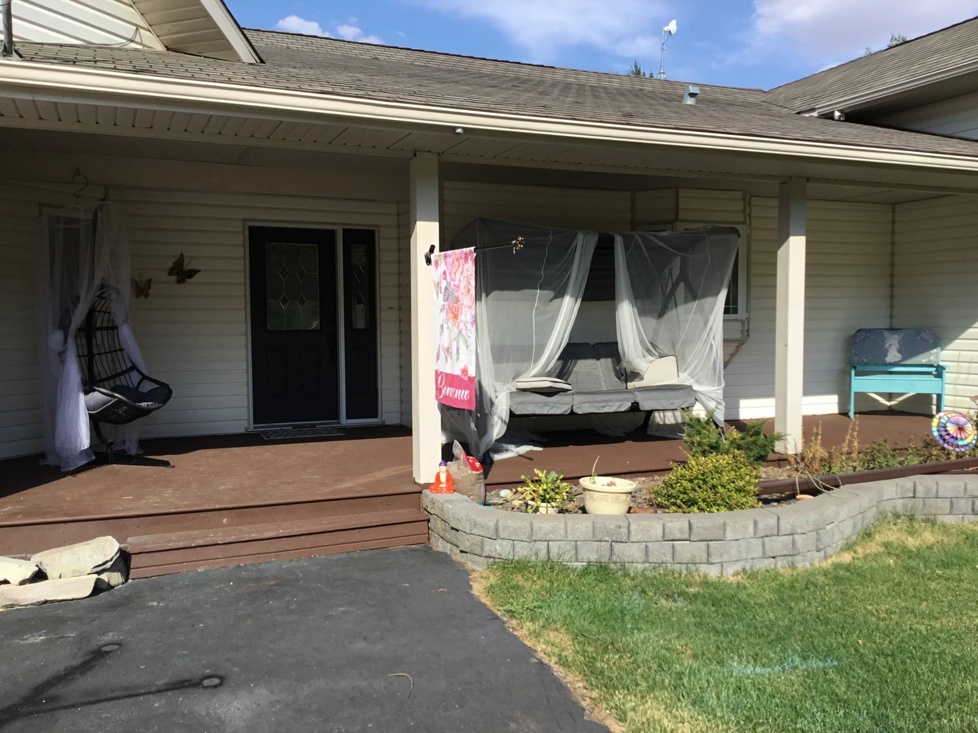 Front porch with swing bed under netting, hanging chair, bench and garden beds.