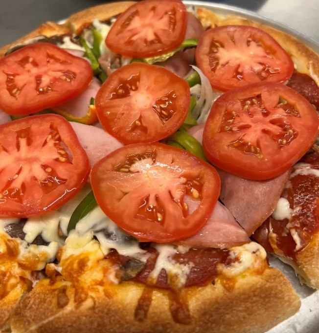 Close-up of pizza topped with tomato slices, meats, cheese, and green peppers