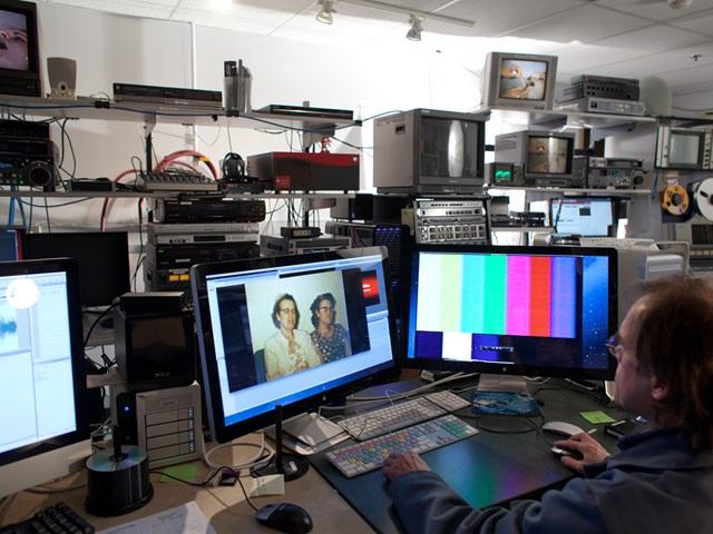 Person working at desk with monitors and media equipment at Provincial Archives of Alberta.