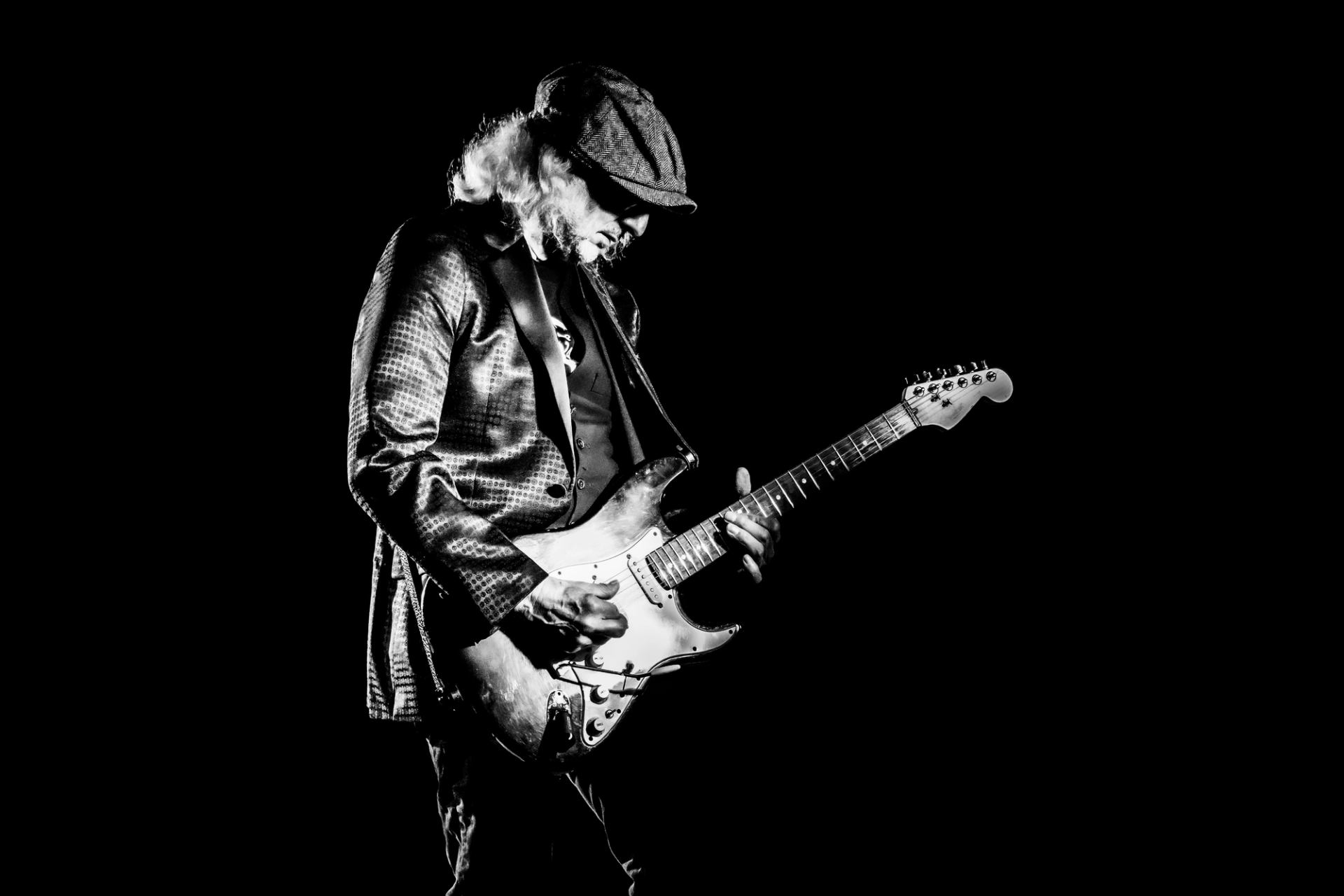 Black and white image of a man in a cap playing an electric guitar.