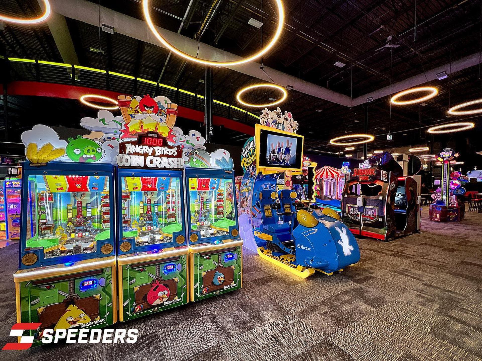 Indoor arcade with Angry Birds machines, racing simulators and glowing circular ceiling lights.