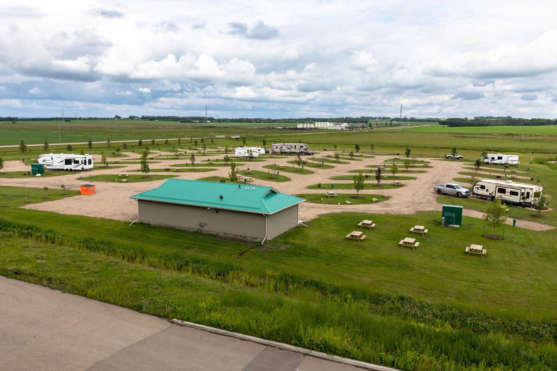 Wide view of RV park with gravel lots, green roof building, and picnic tables.