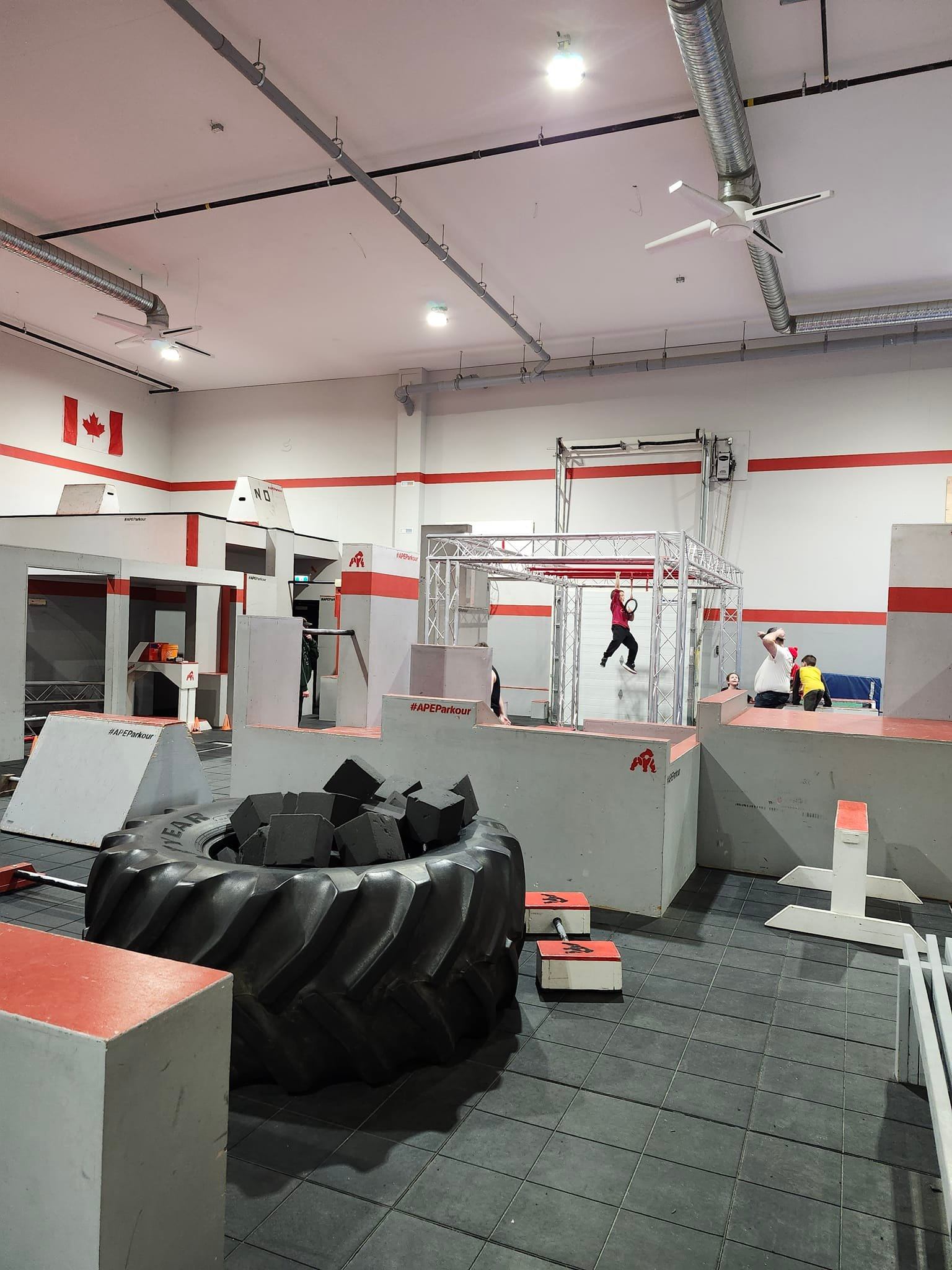 Indoor ninja warrior obstacle course with foam pit, ramps, and metal frame with athletes jumping.