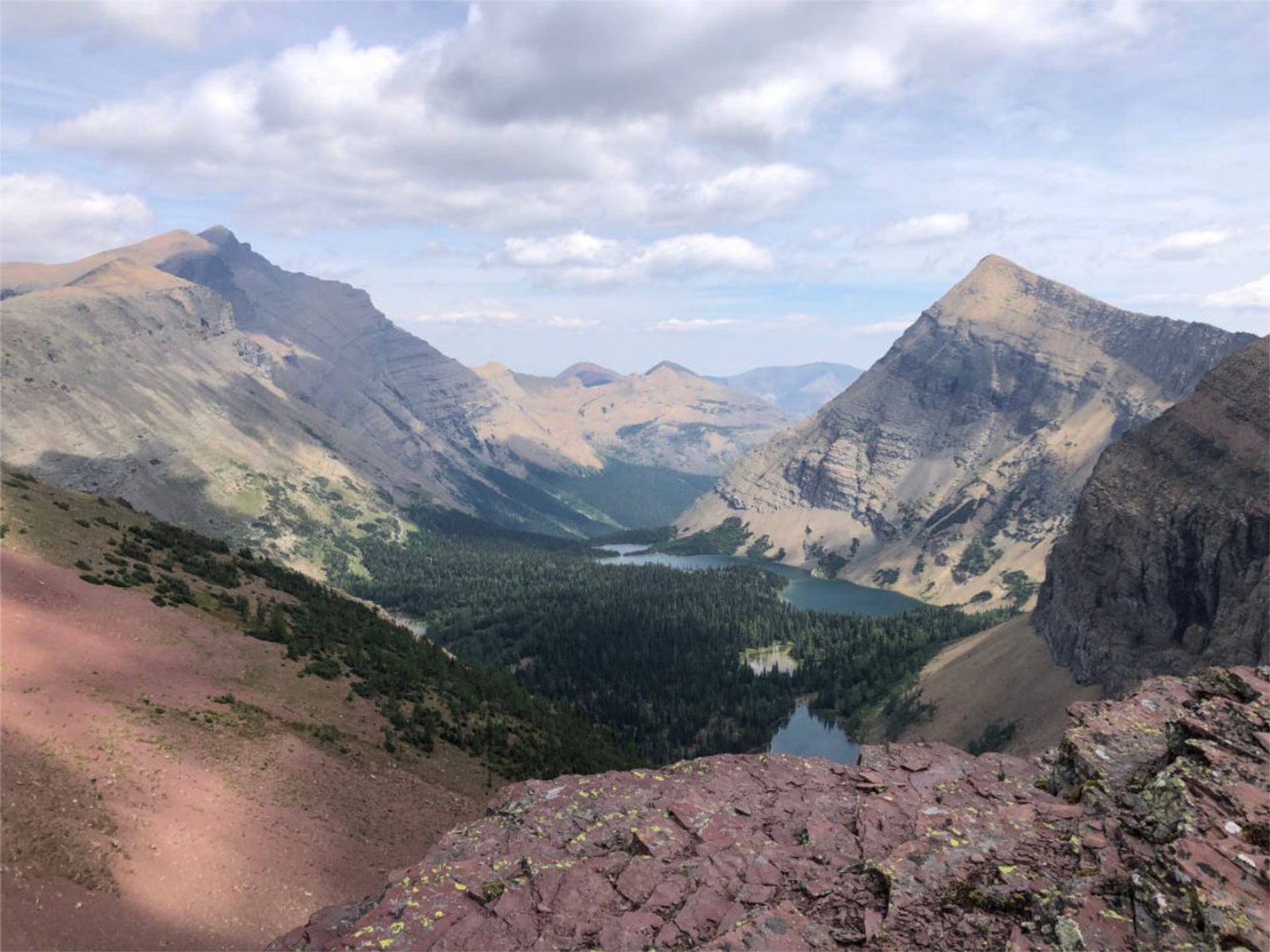 Mountain valley with layered rock peaks and lakes viewed from a high ridge.