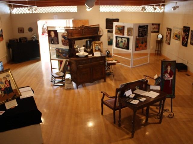 Art gallery with paintings on walls and easels in a wood-floored room.