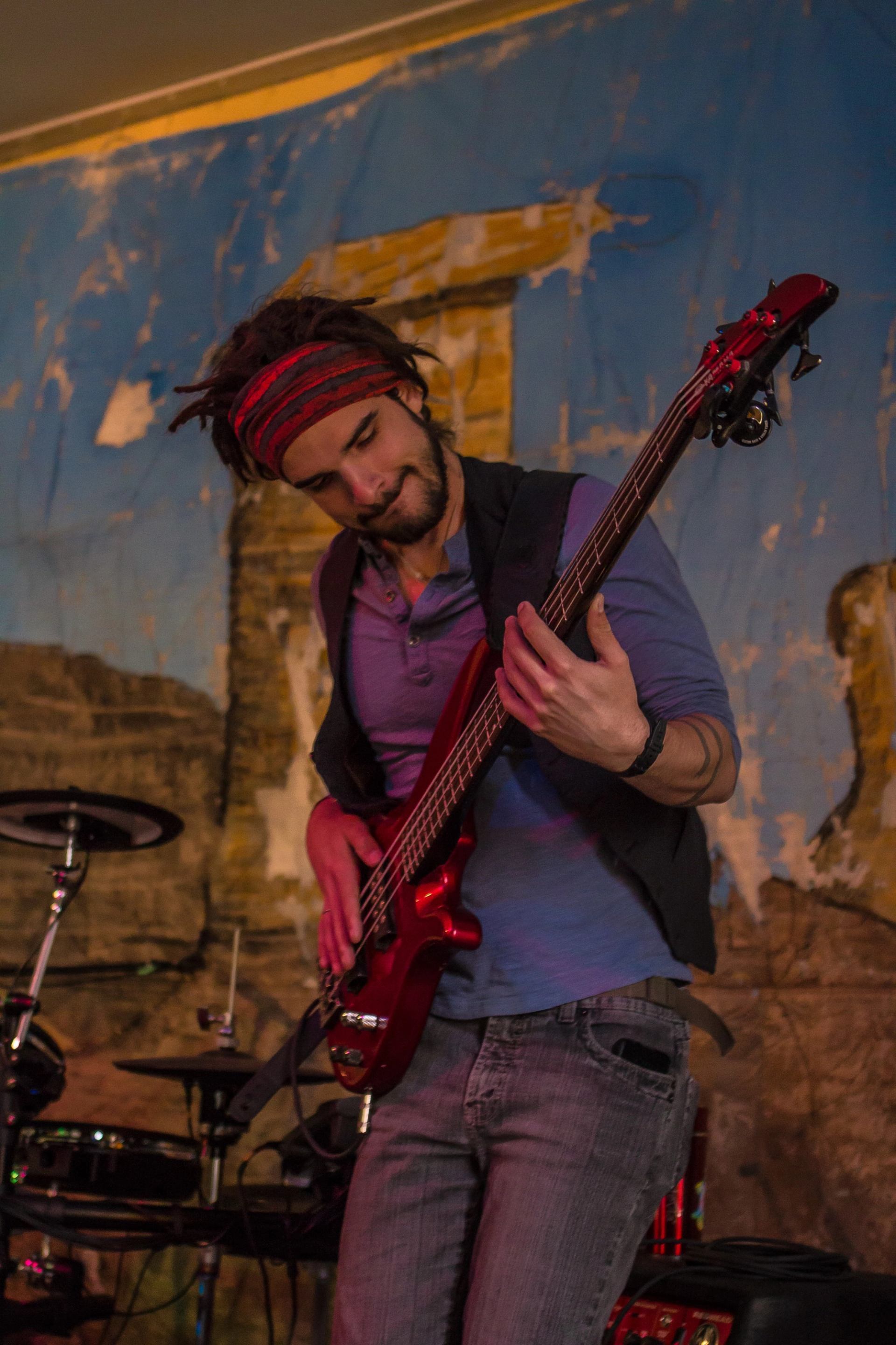 Musician playing a red electric bass guitar on stage.
