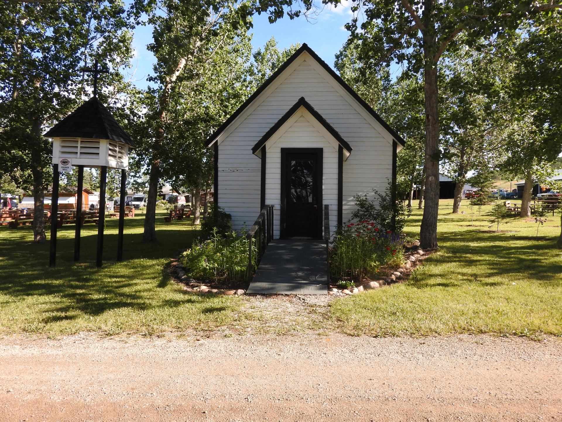 White wooden museum building with black trim, doorway, and surrounding trees and grass.
