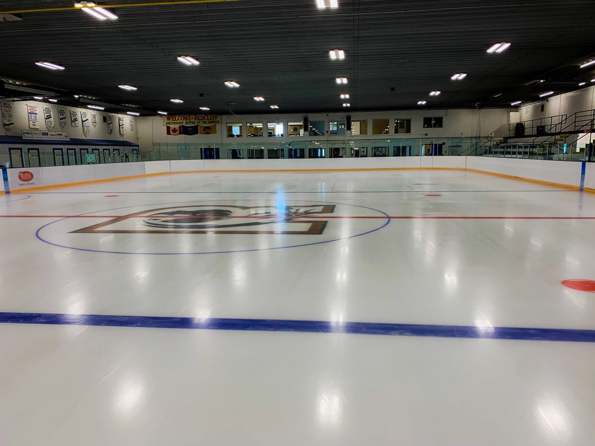 Clean ice rink with center logo, boards, and ceiling lights