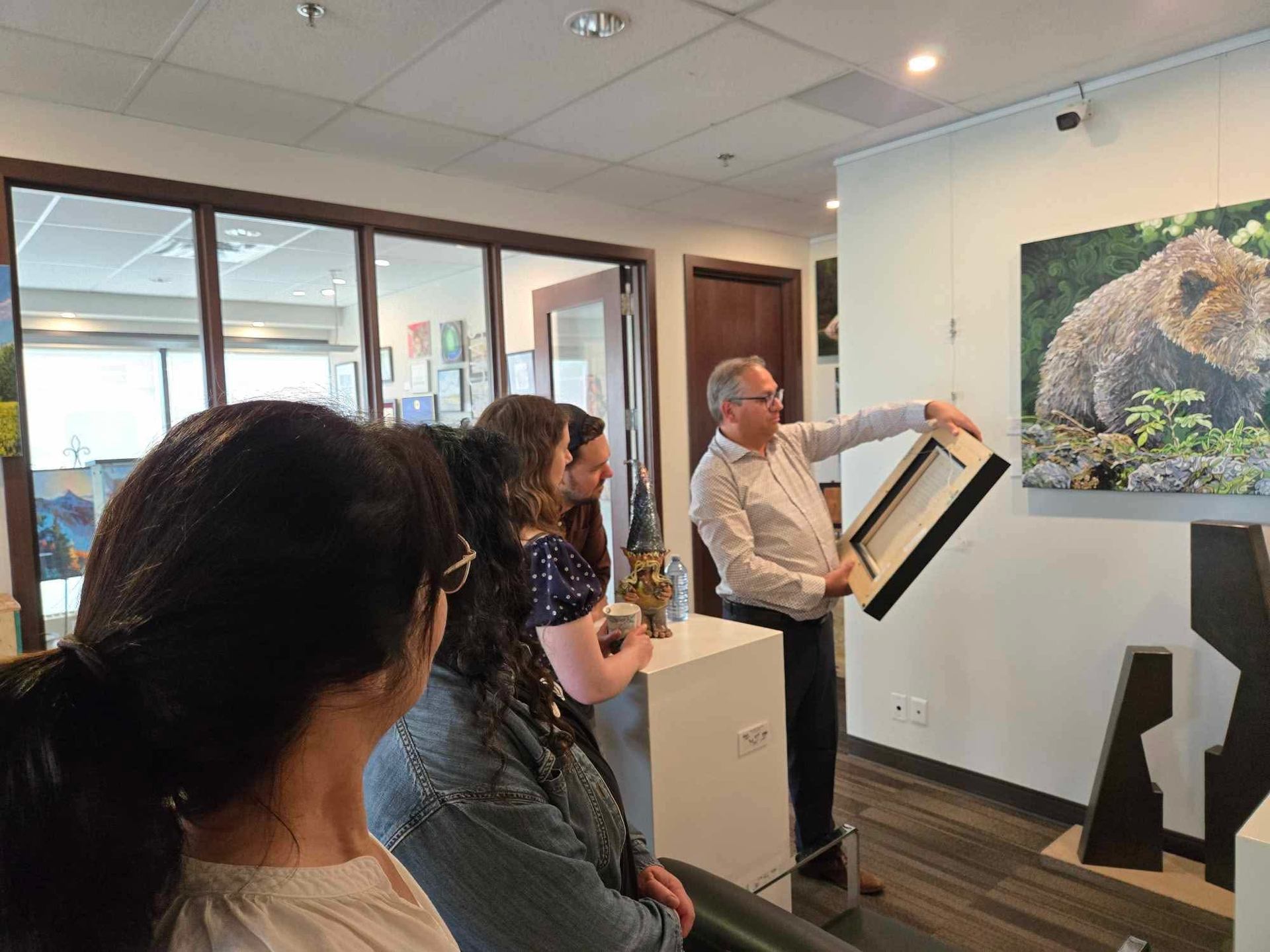 People look at a painting as a man presents art inside an art gallery.