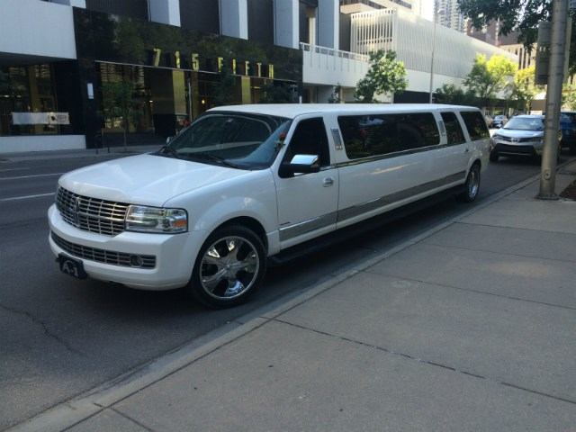 White limo with chrome wheels parked on city street with buildings and trees in the background.