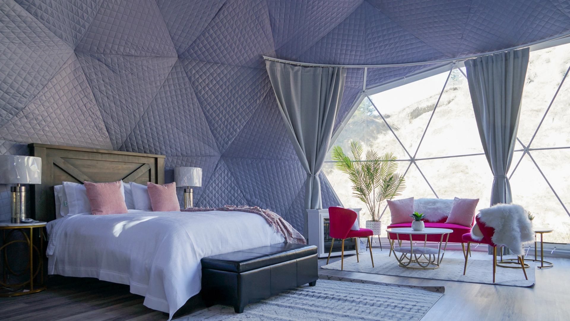 The interior of a glamping dome with a bed, couch, coffee table, and large window.