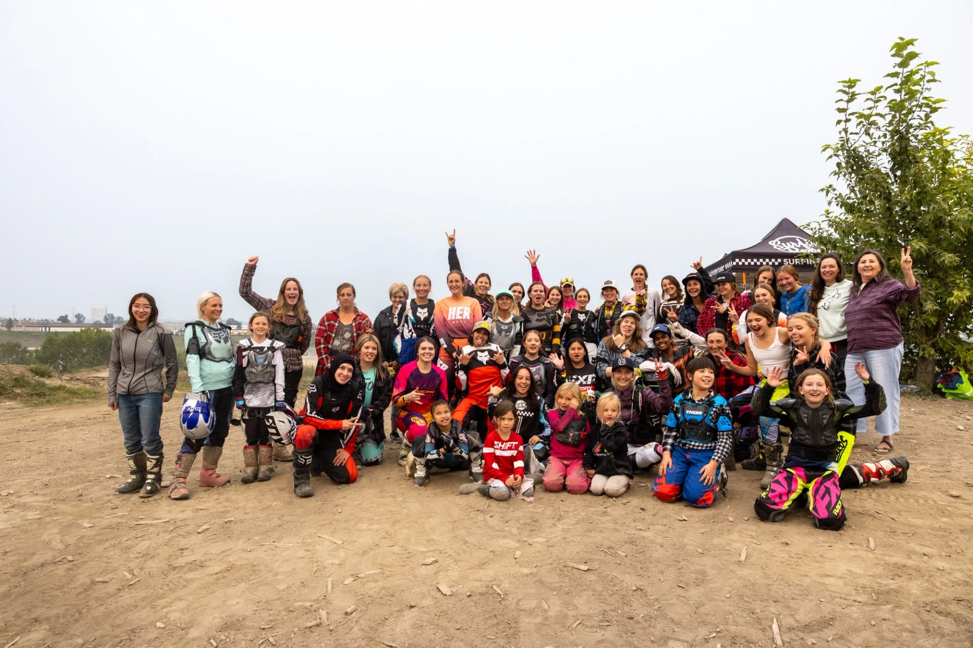Group of bikers and families gathered outdoors at a dirt event site.