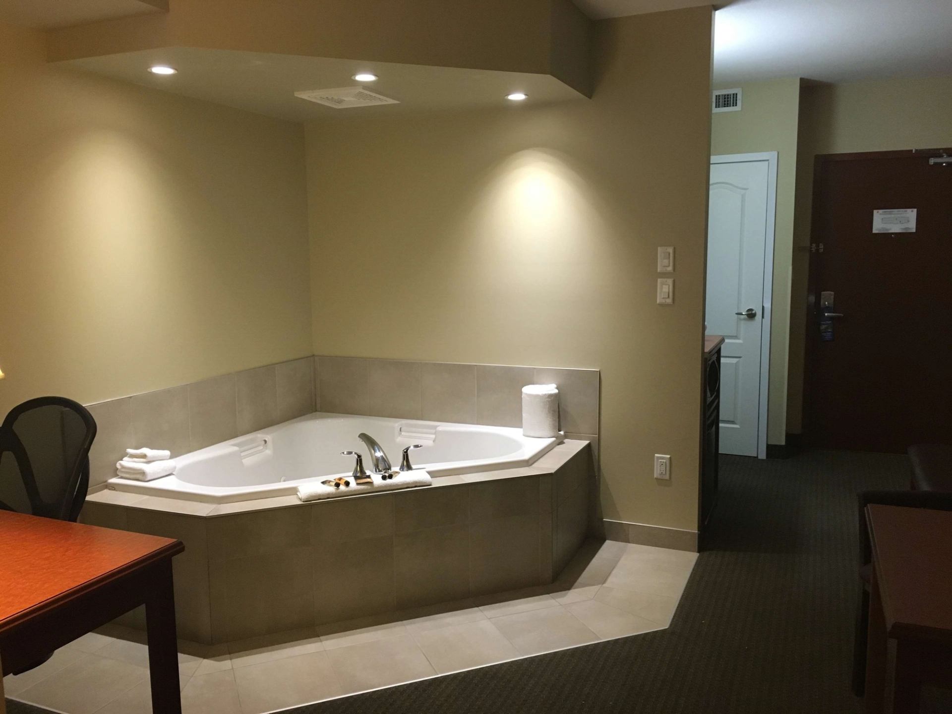 Corner tub with folded towels beside table and doorway in hotel suite.