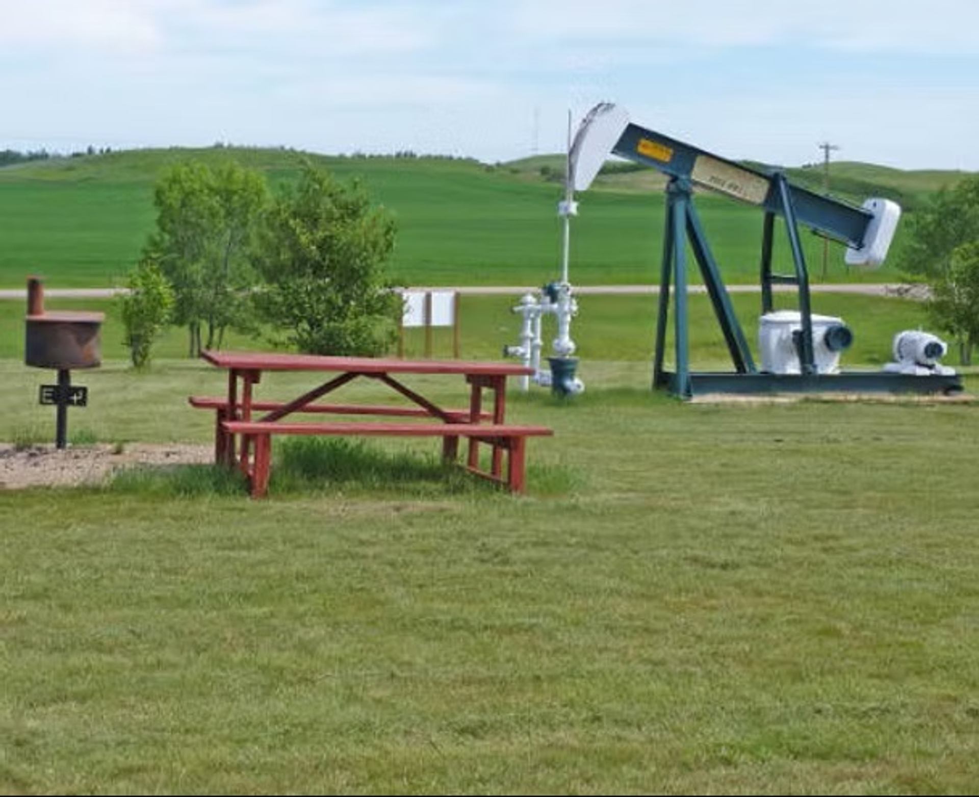A picnic table and barbecue stand on a grassy campsite with rolling hills and open countryside.