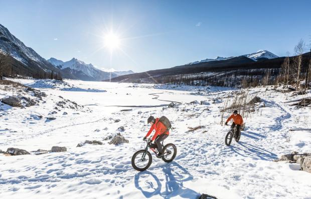 Two people fatbiking on a frozen Maligne Lake on sunny winter's day in Jasper National Park.