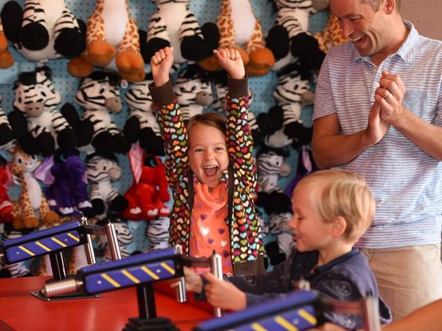 A child cheers and man applauds while another child plays a carnival game.