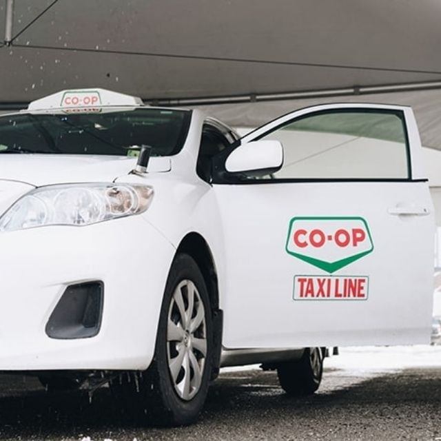White Alberta Co-op Taxi with open door and visible logo on wet pavement.