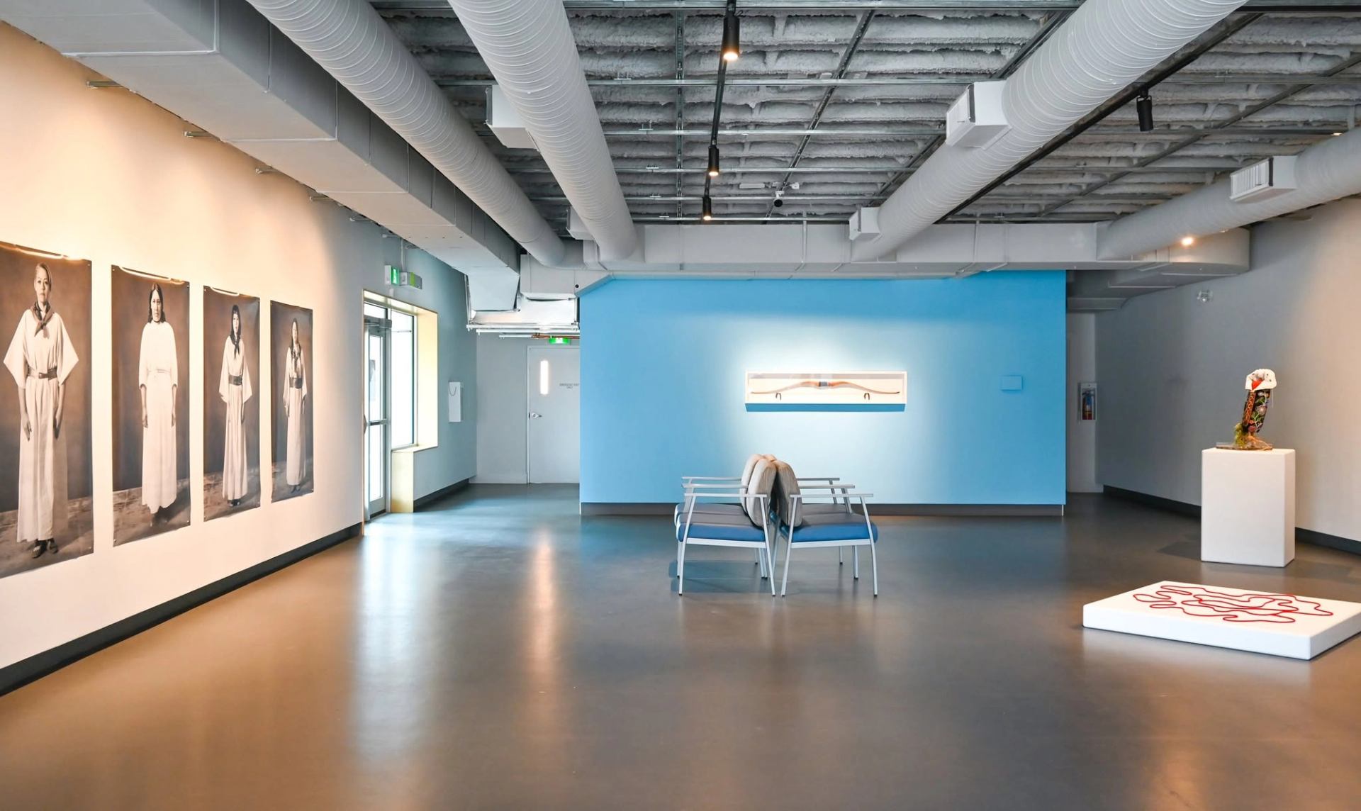 Contemporary gallery interior with portraits, sculptures, blue accent wall and central seating.