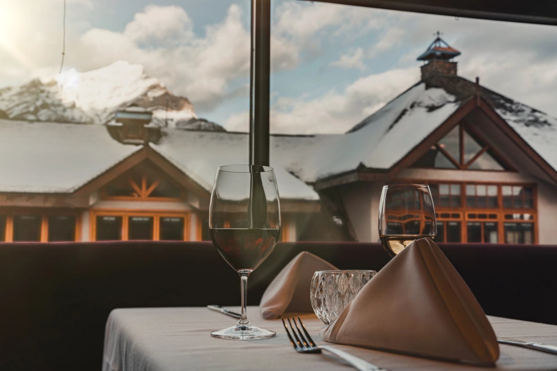 A white linen covered table is set with 2 glasses of wine. The window has views of Cascade mountain.
