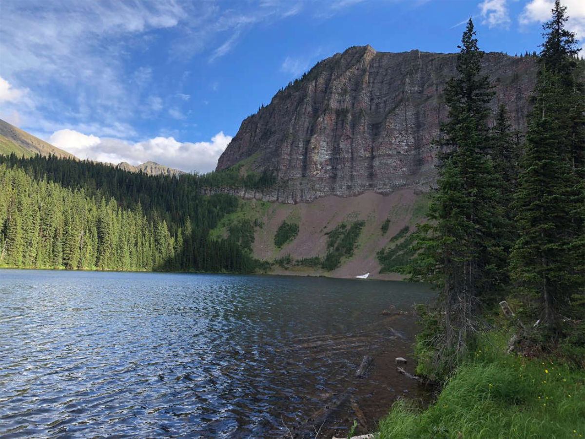 A peaceful mountain lake bordered by forests and rocky cliffs under a blue sky.