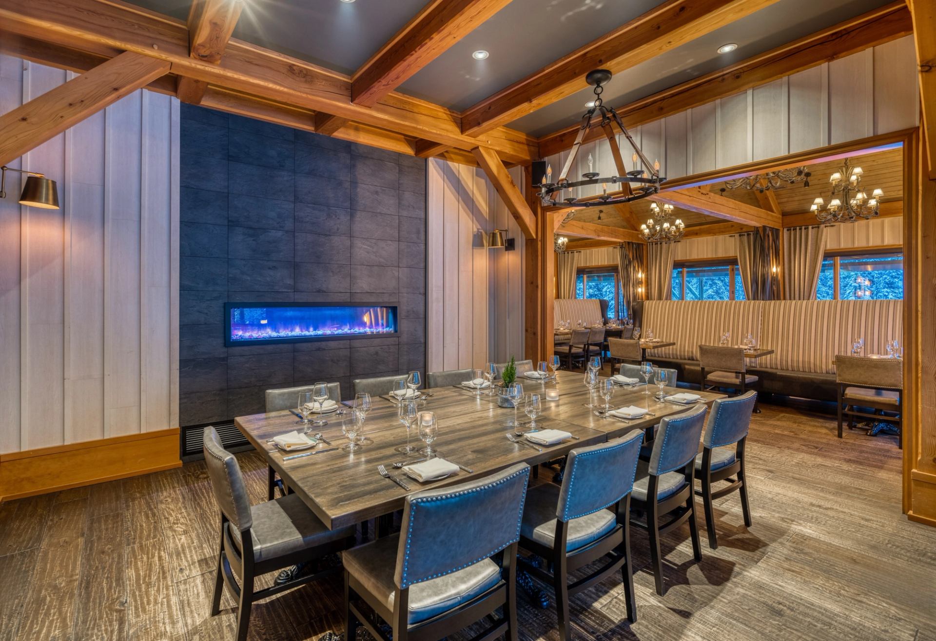 Dining room with long wooden table, blue chairs and modern linear fireplace.