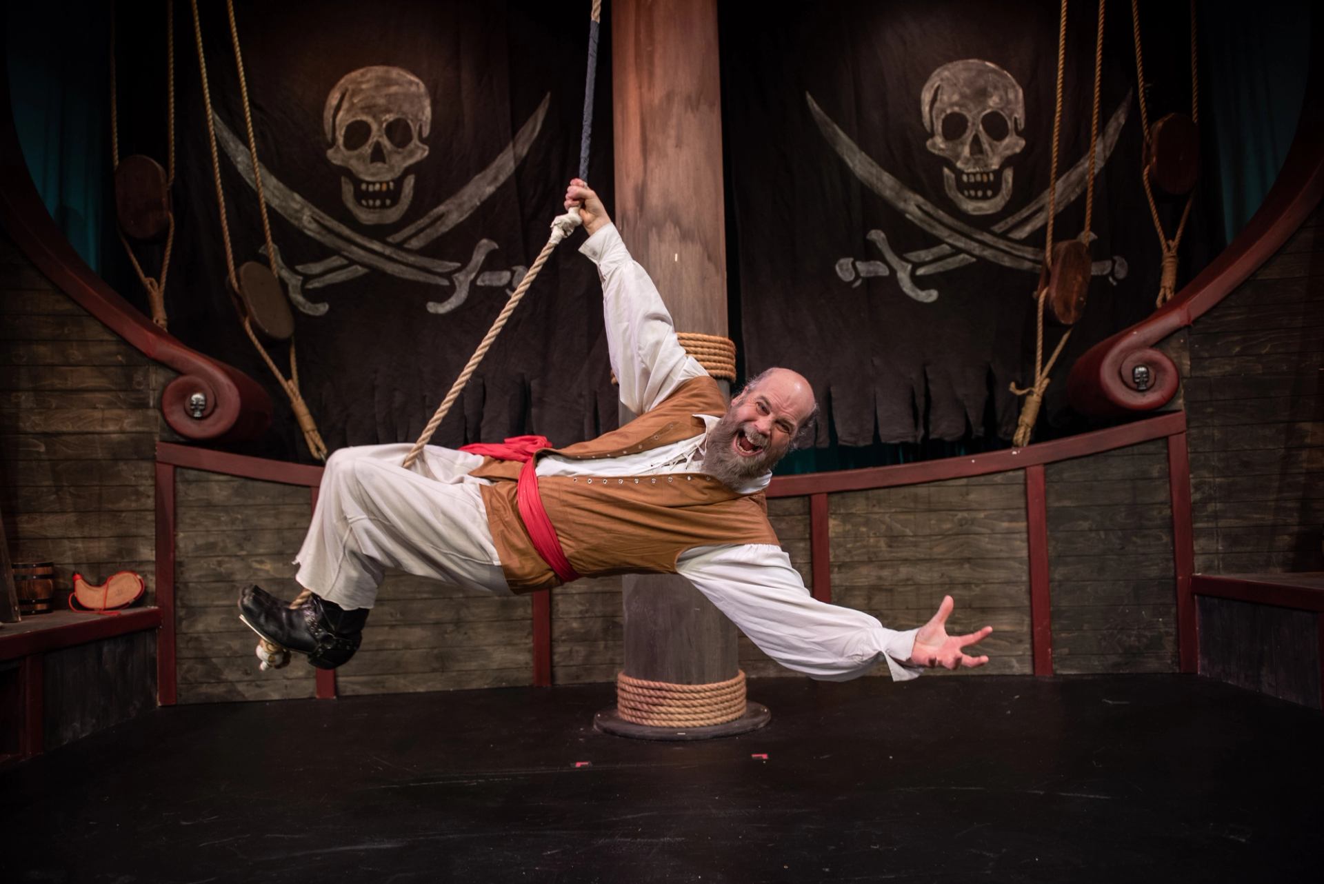 Pirate actor hanging from a rope on a ship set with skull backdrop