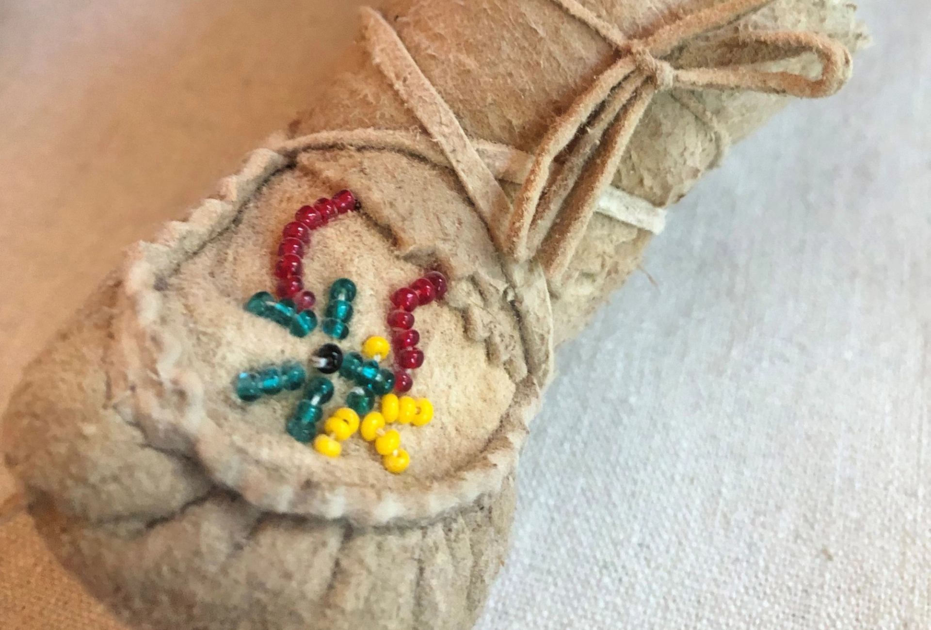 Beaded design on tan leather moccasin with red, teal, yellow and black beads.