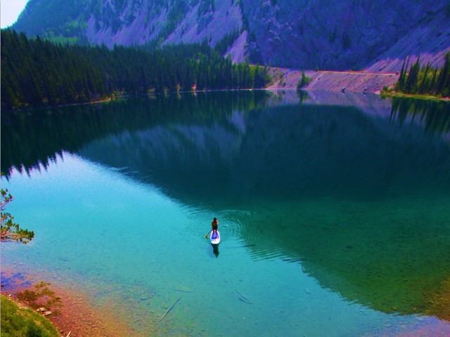 Person paddling on a calm lake surrounded by forest and mountains.