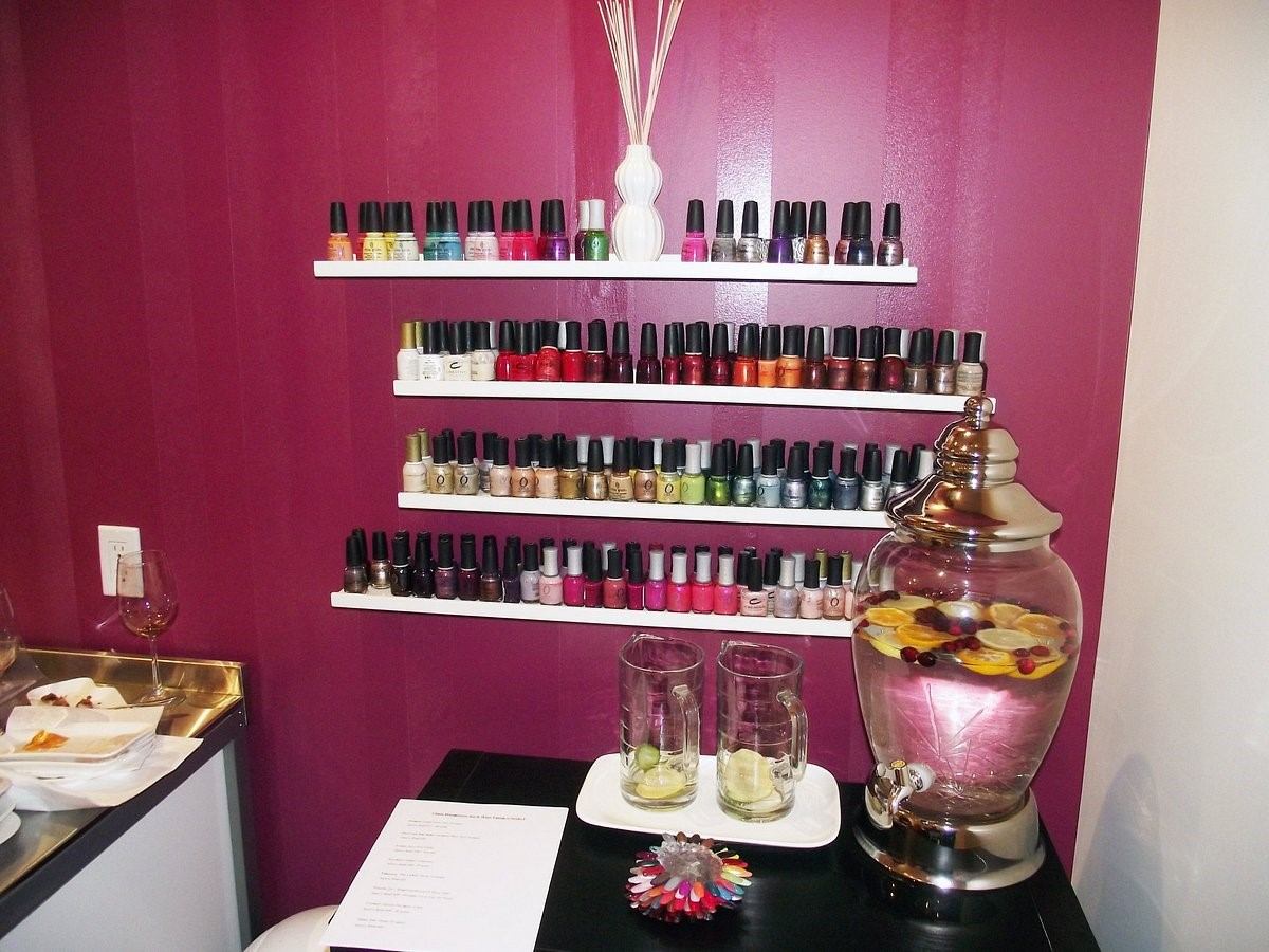 Nail polish bottles on shelves, with flower accents and drink glasses on a spa table.