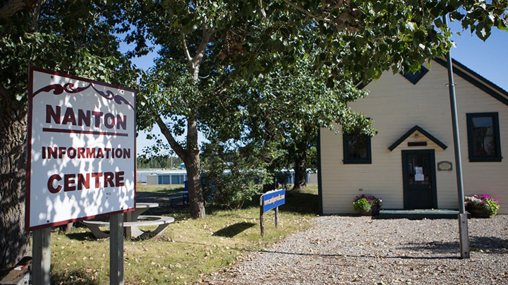 Nanton Information Centre sign beside a cream building shaded by leafy trees.