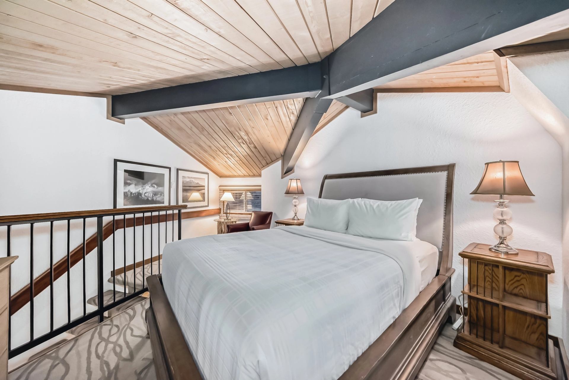 Loft-style bedroom featuring a queen bed, wooden ceiling beams, and bedside lamps