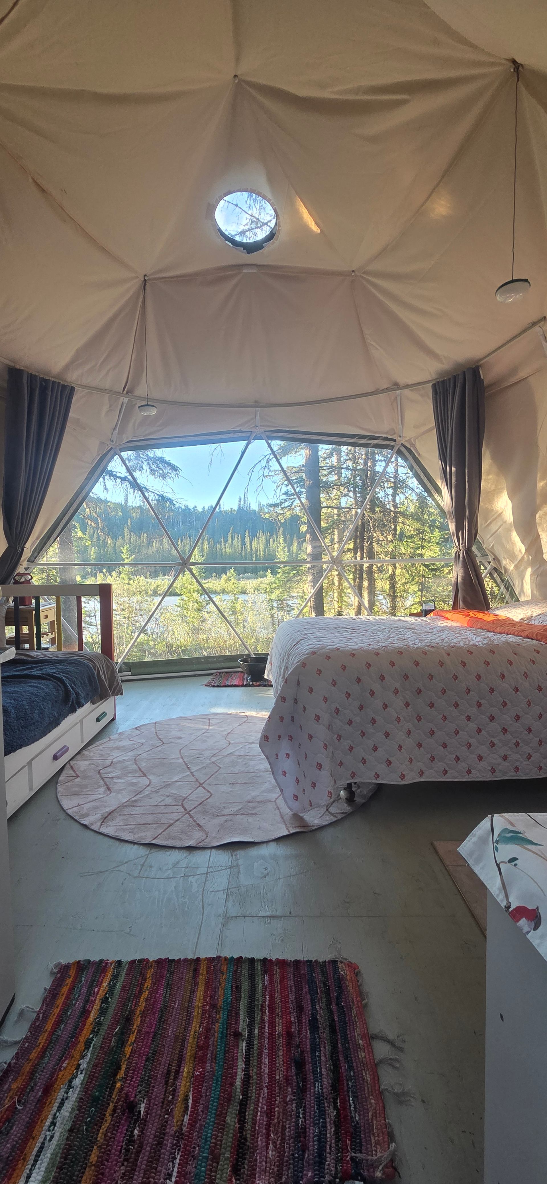 Geodome interior showing a double bed, trundle bed, and view of the river.