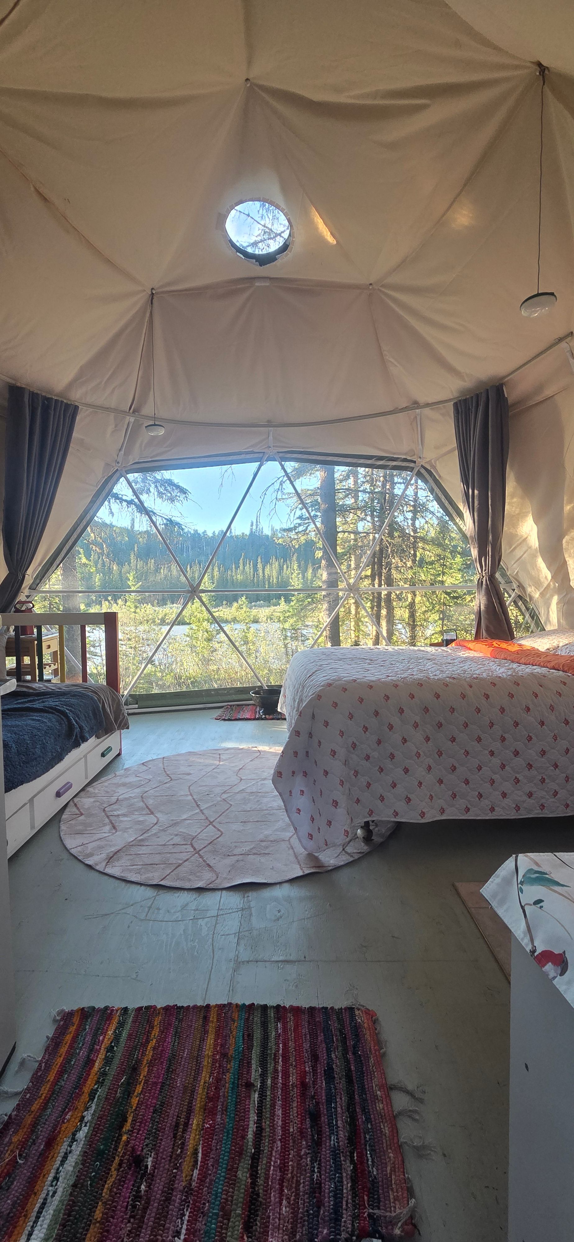 Geodome interior showing a double bed, trundle bed, and view of the river.