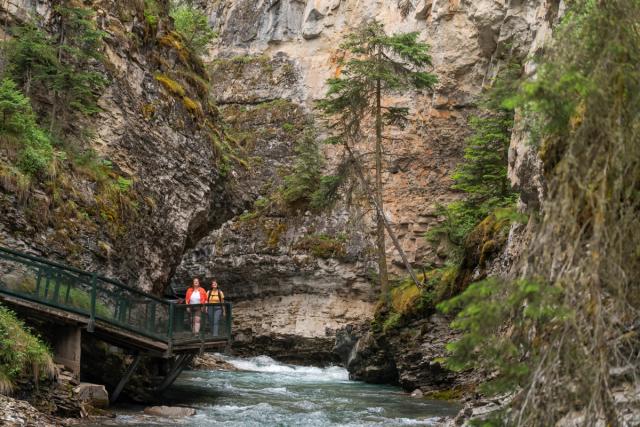 A shot of the immense Johnston Canyon with a couple walking along the boardwalk.