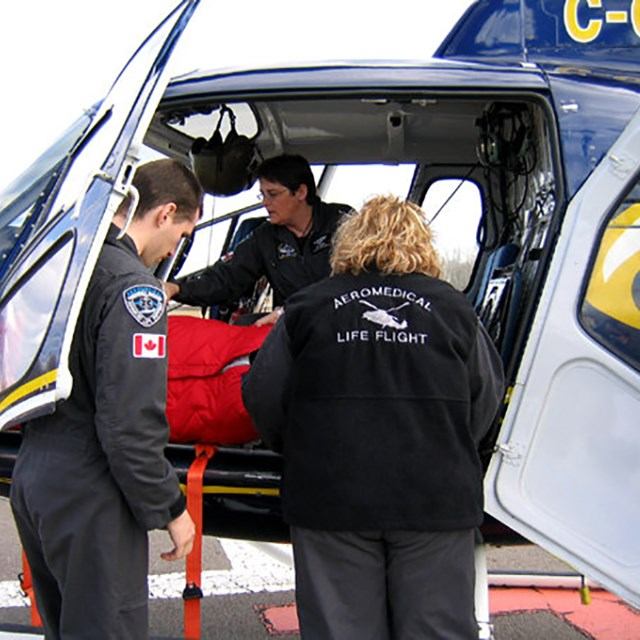 Crew loads red stretcher into helicopter cabin, Aeromedical Life Flight jacket visible.