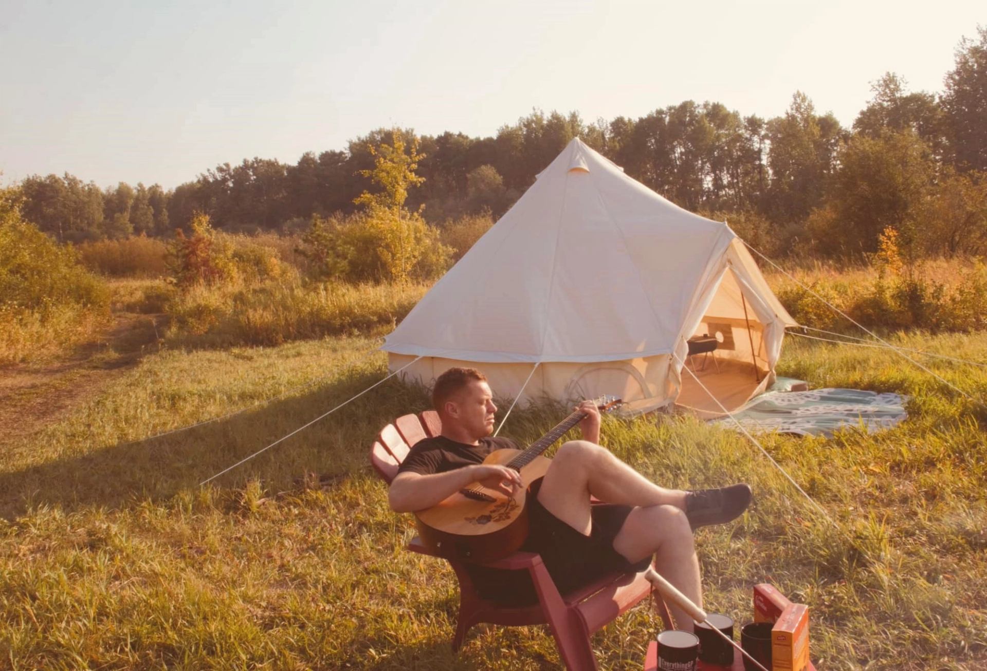 Canvas tent in grassy field with person playing guitar nearby