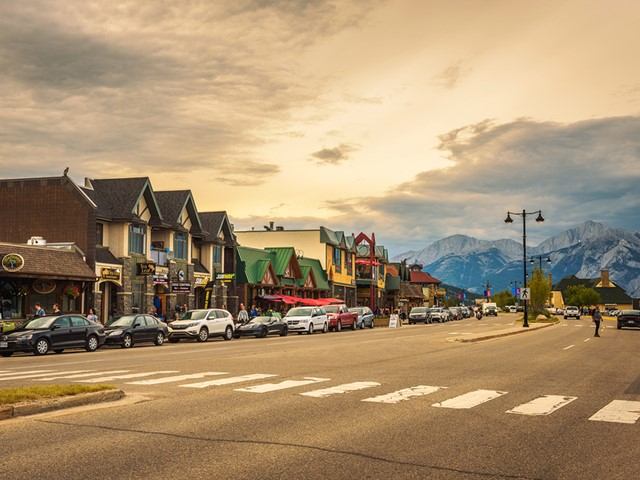 Small town main street with shops, parked cars and distant snow-capped mountains.
