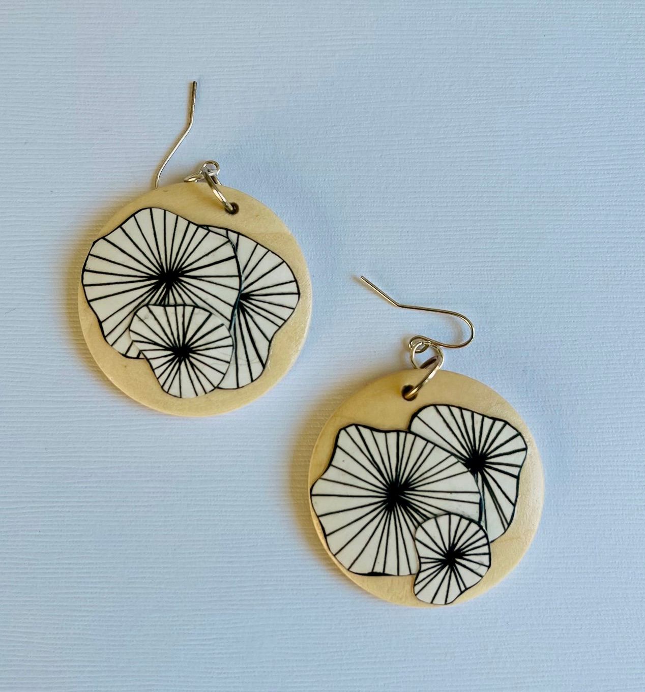 Round earrings with floral line art on a light base.