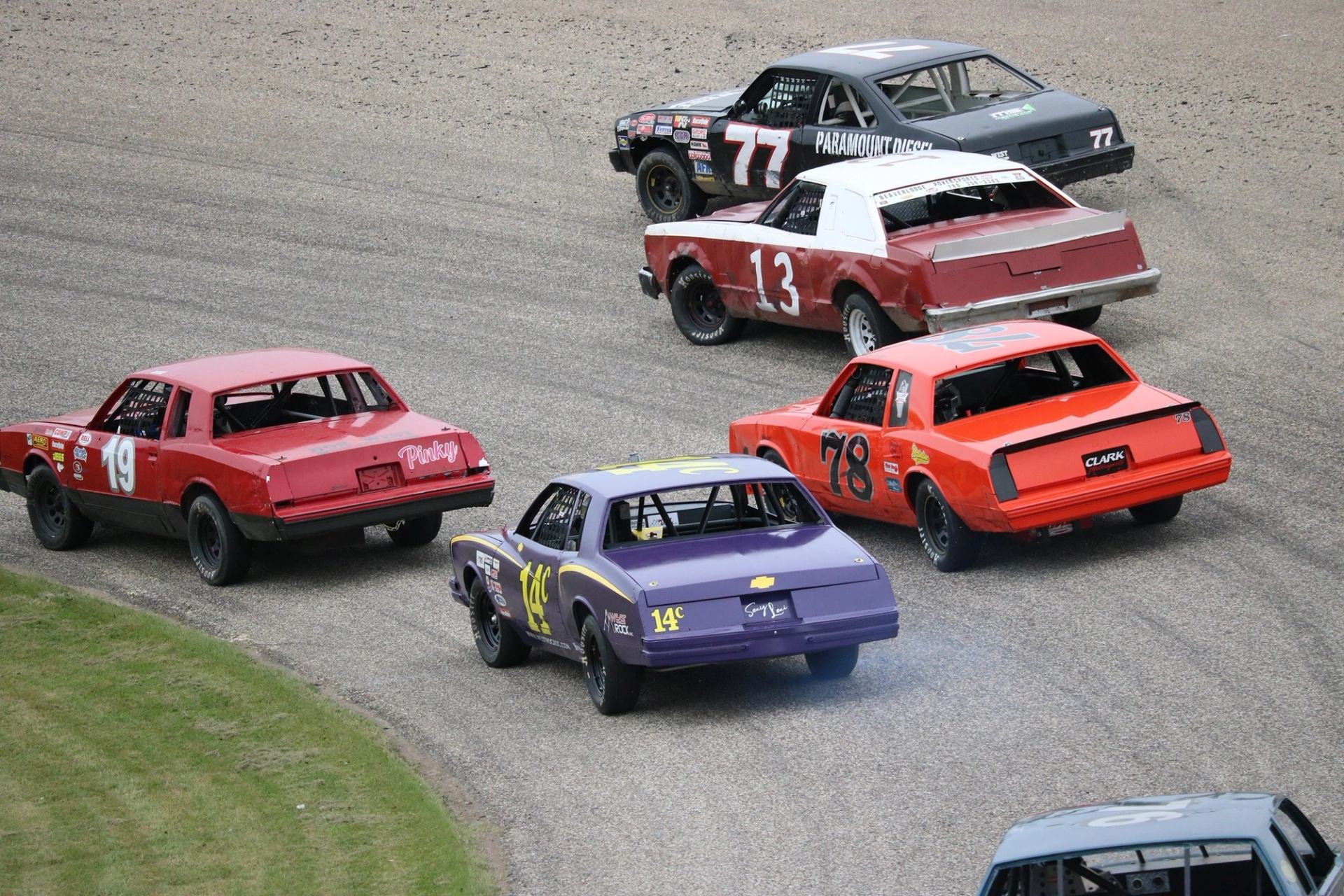 Several stock cars navigating a turn on the paved track at the speedway.