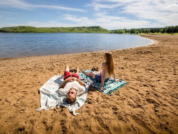 Couple on a beach lying on their towels in Cypress Hills Provincial Park.