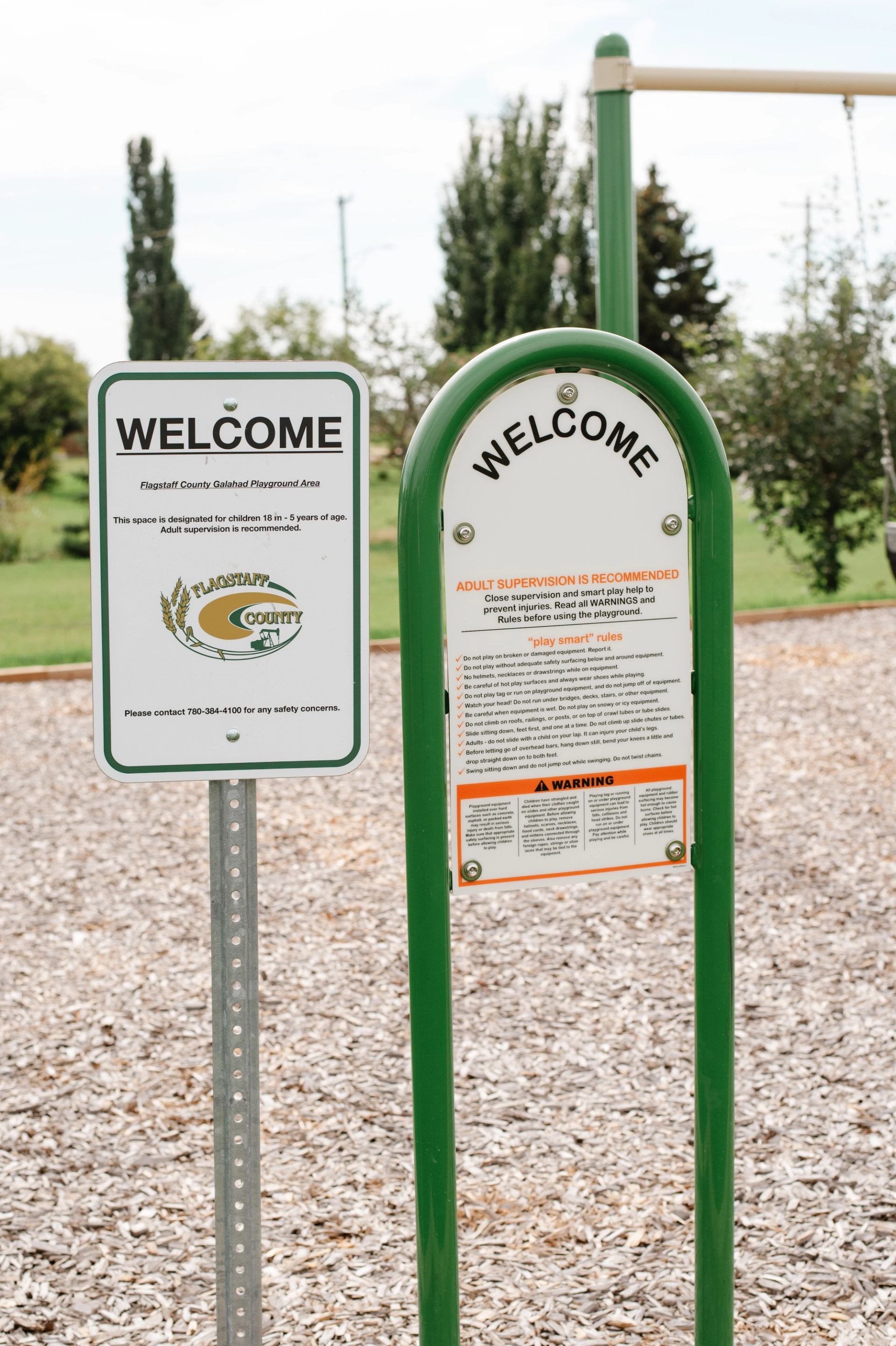 Playground welcome signs with safety rules in Flagstaff County, surrounded by trees.