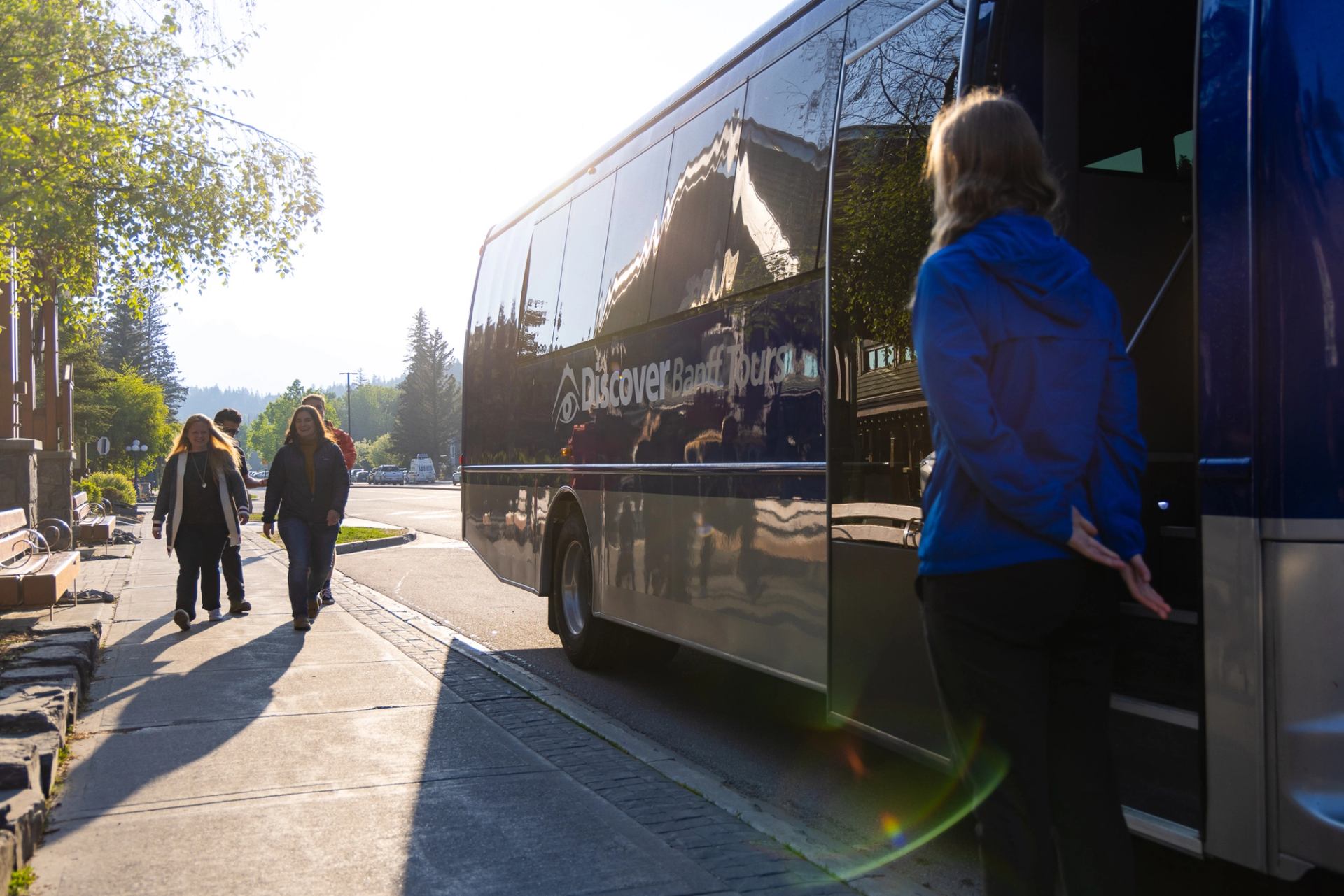 Tour bus labelled Discover Banff Tours parked as people walk along nearby sidewalk.