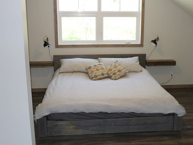 Cozy bedroom with a rustic wooden bed frame, white bedding, decorative pillows, and large window.