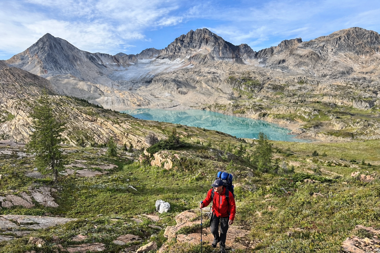 Backpacker approaches turquoise lake amid rocky alpine terrain